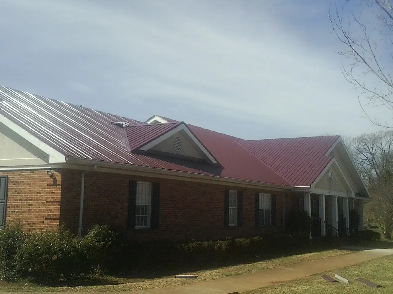 Red metal roof with gabled entries on a long brick building, from a Hail Damage Roof Repair job in Ault