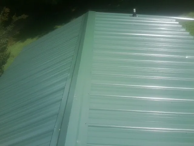 New green metal panels meeting at the ridge of a roof — Flat Roof Repair work by our crew in Ault