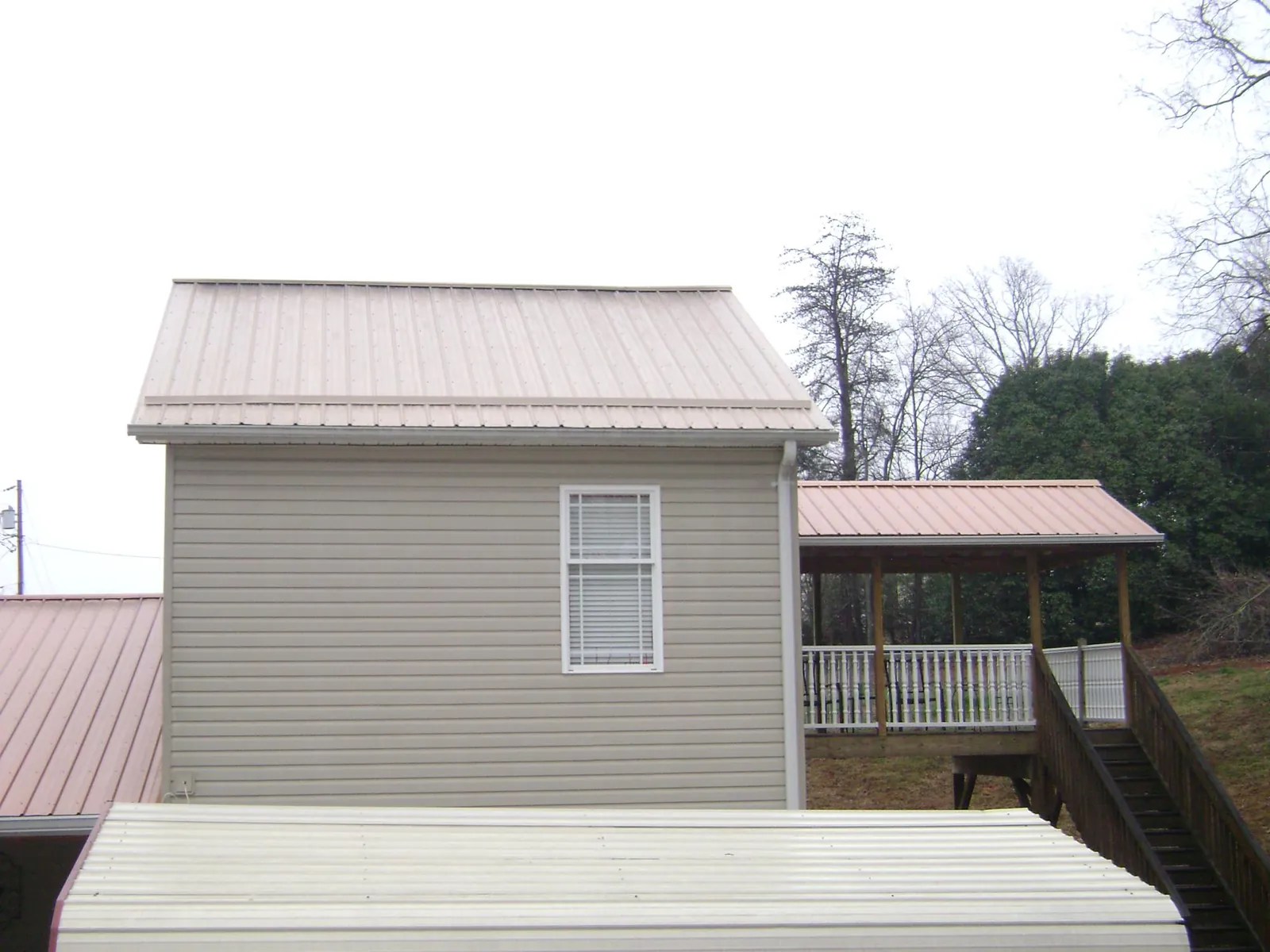 Tan metal roofs on a two story addition and attached porch, from a Roof Replacement job in Ault